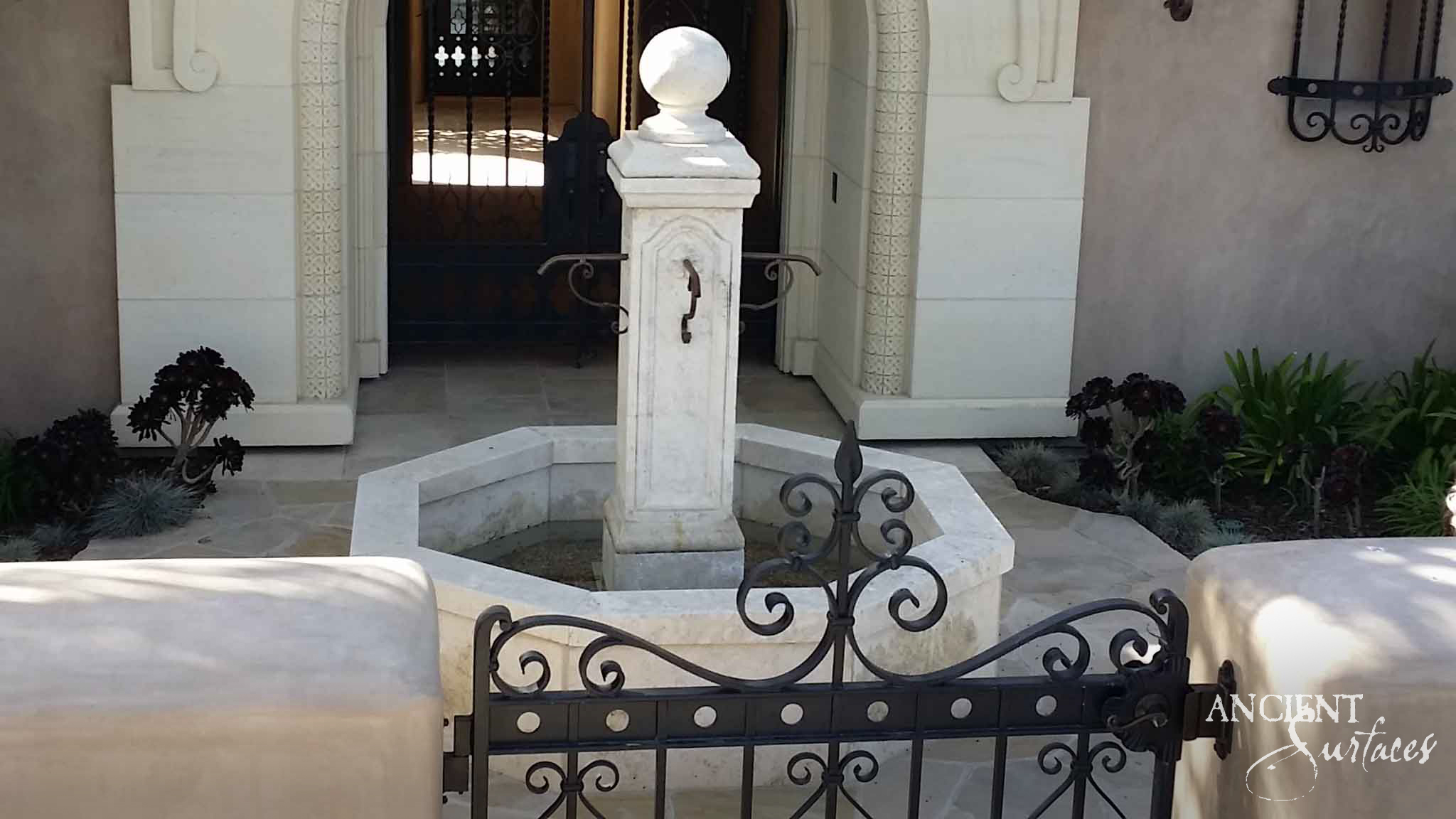 Pale reclaimed limestone pool fountain with an ogee arched pillar, ball finial and iron spout standing in a low octagonal pool at a house entrance