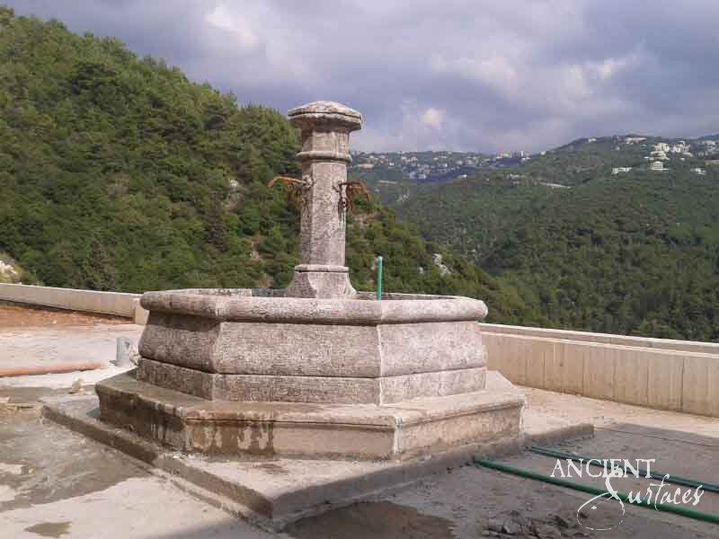 Reclaimed limestone pool fountain with a fluted round pillar and iron spouts raised on a stepped stone plinth above an open terrace