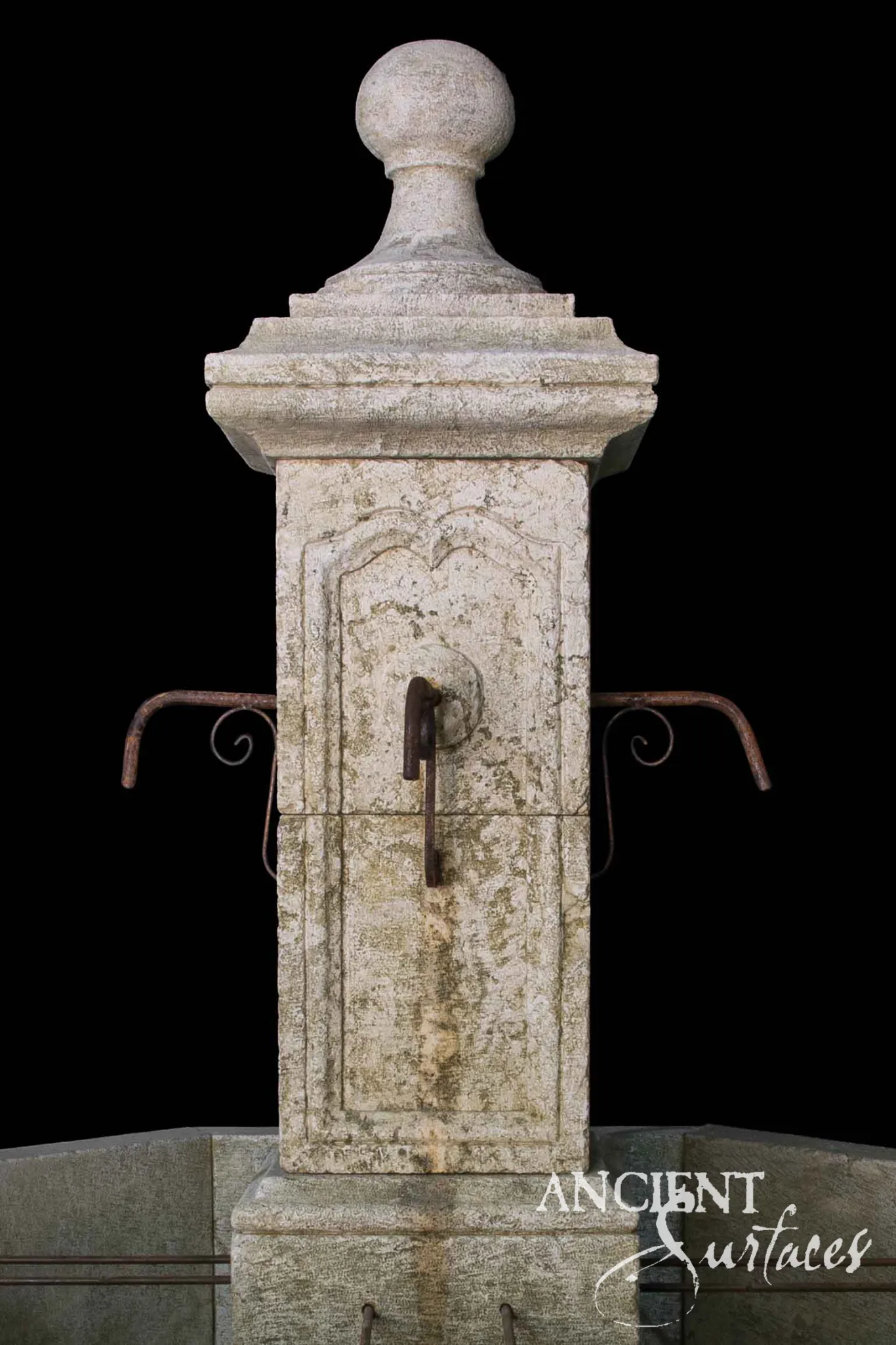 Close view of a reclaimed limestone pool fountain pillar with a carved ogee arched panel, iron spout, scrolled brackets and a ball finial