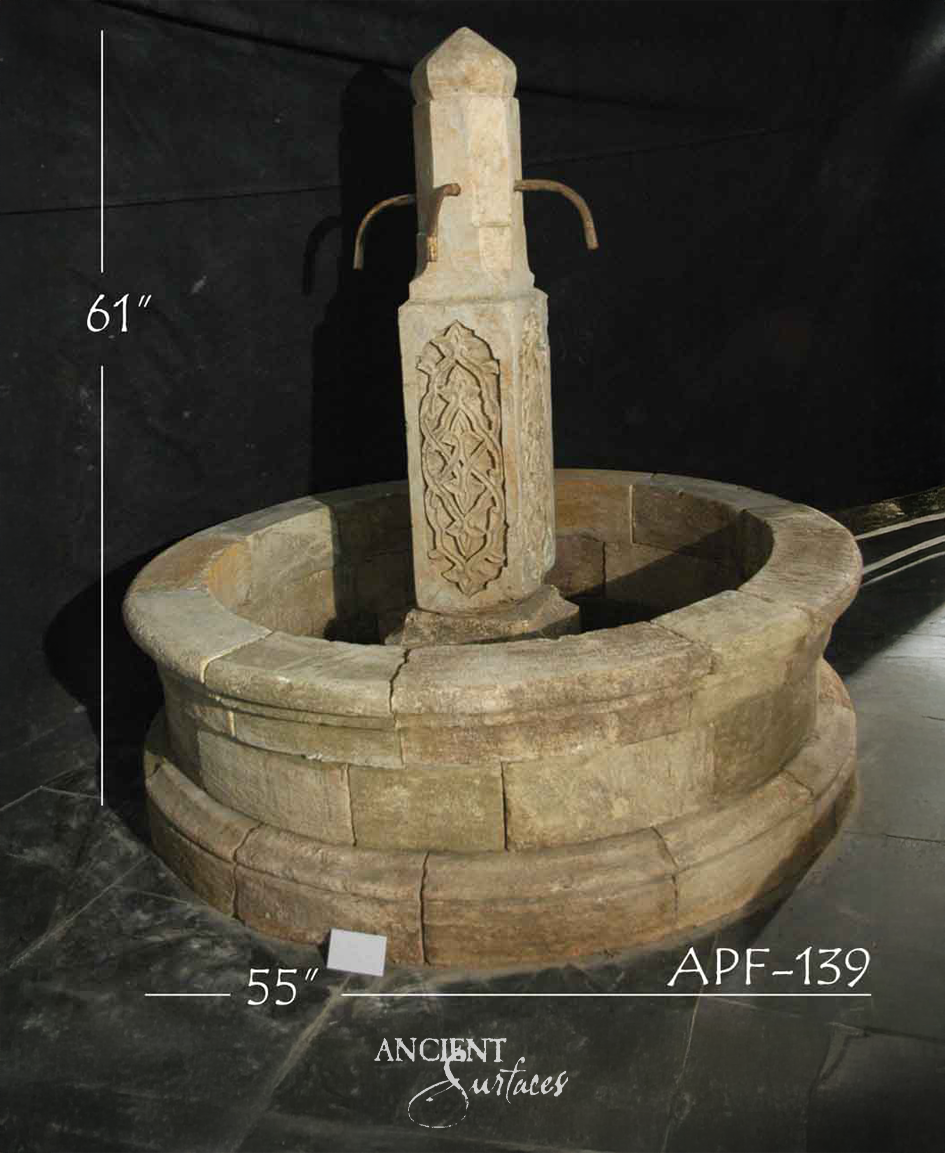 Round reclaimed limestone pool fountain with a tapering pillar carved with an interlaced strapwork panel and two curved iron spout arms
