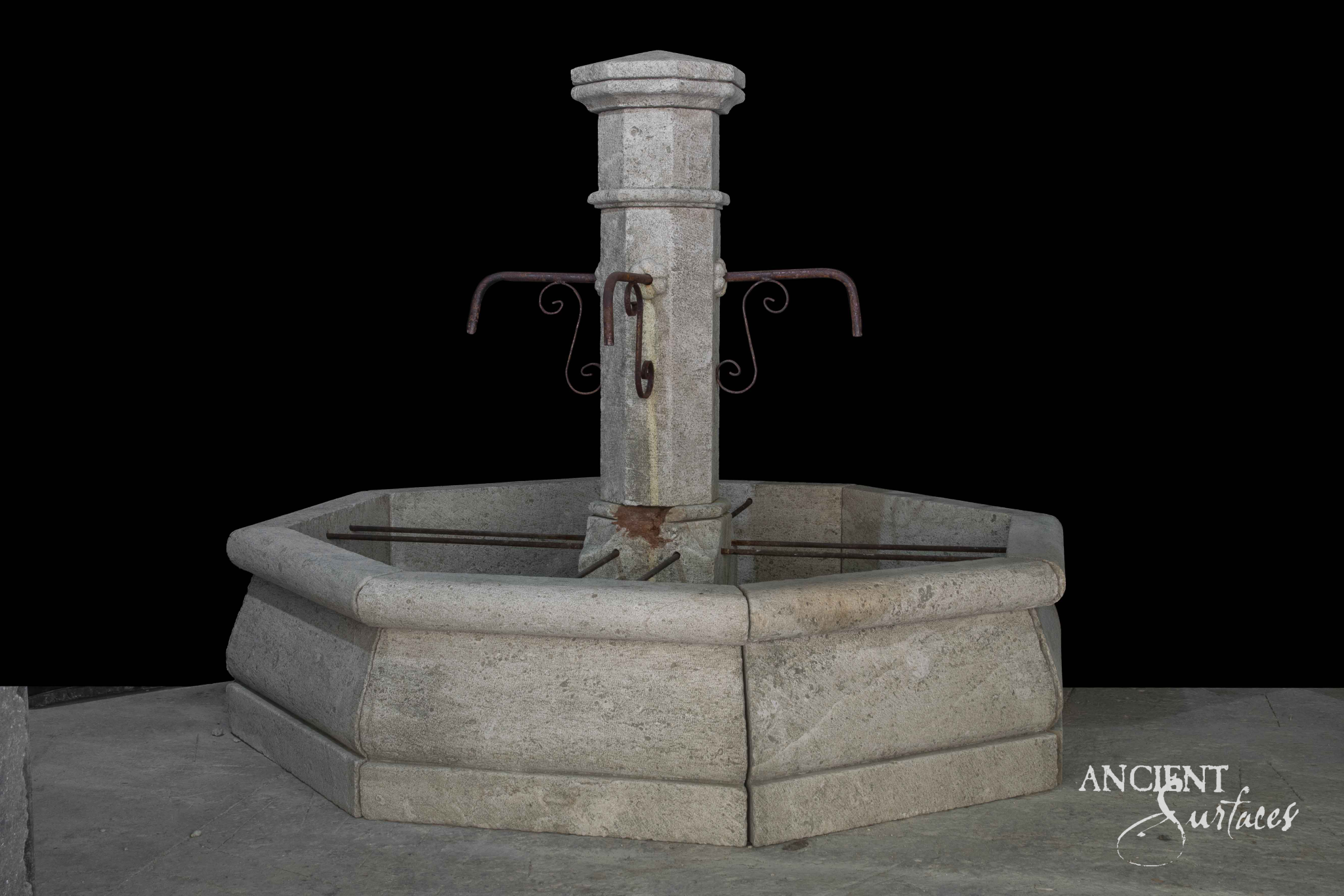 Pale reclaimed limestone pool fountain in three quarter view with scrolled iron spouts, an ochre stain down the pillar and an octagonal block built pool